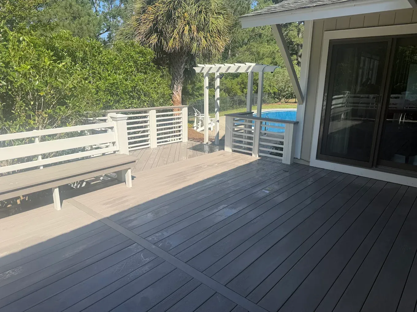 Gray composite deck with white bench and railing overlooking a pool.