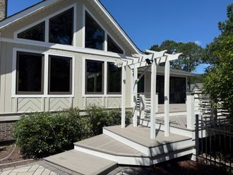 Tan house with large windows, deck, and white pergola; sunny day.