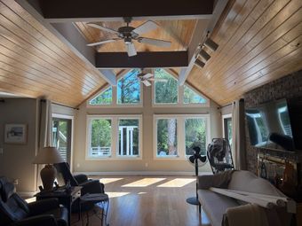 Bright living room with high wood ceiling, large windows, and a stone fireplace.