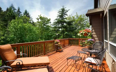 Wooden deck with outdoor furniture and potted plants overlooking trees.