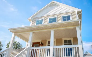 Two-story house with a covered porch, white trim, beige siding, and blue sky.