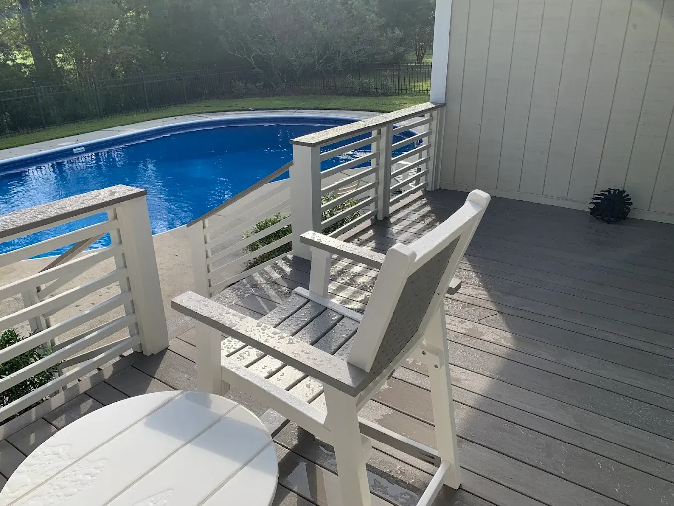 Chair and small table on a deck overlooking a swimming pool.