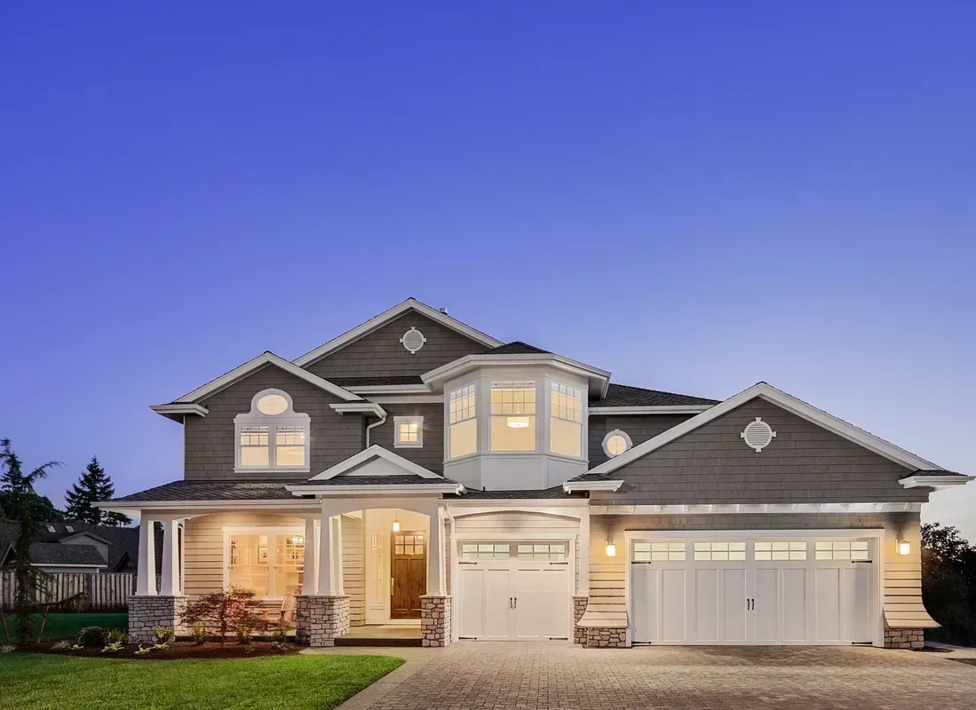 Elegant two-story home with beige siding, white trim, and a circular window tower, at dusk.