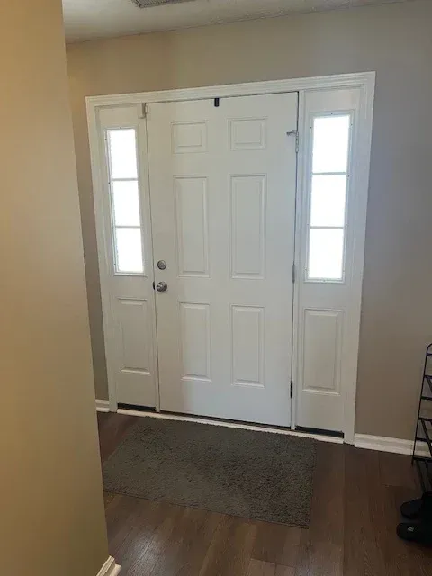 White front door with sidelights, gray mat, and wooden floor. Beige walls.