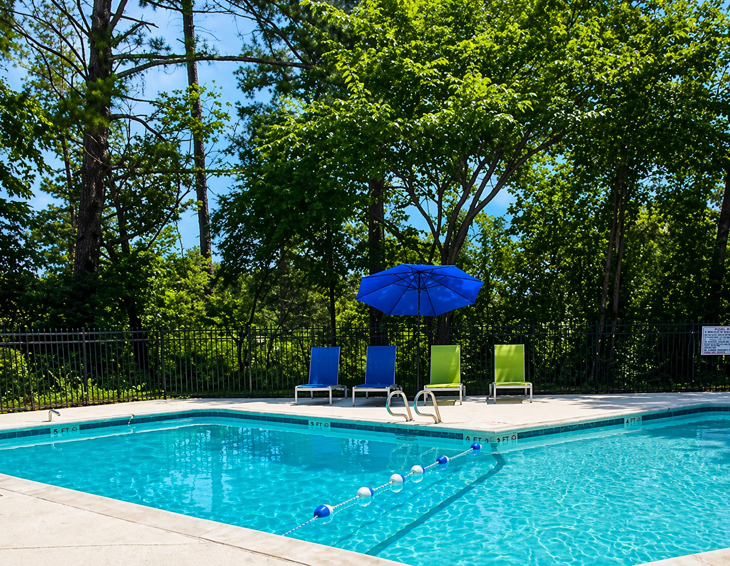 Swimming pool with lounge chairs, blue umbrella, trees, and blue water.