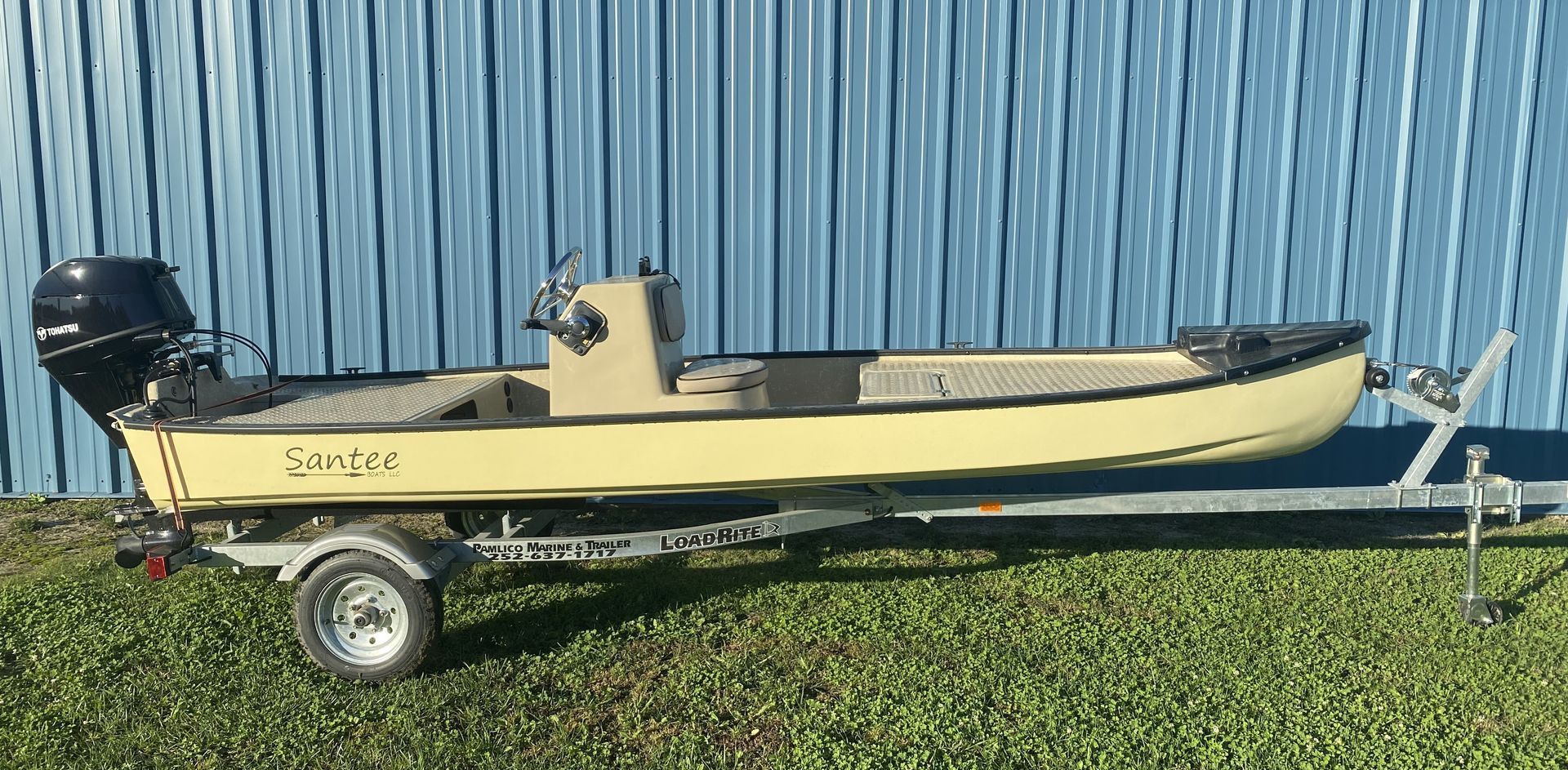 Blue and white motorboat on a trailer, with blue canopy, parked outdoors next to a building.