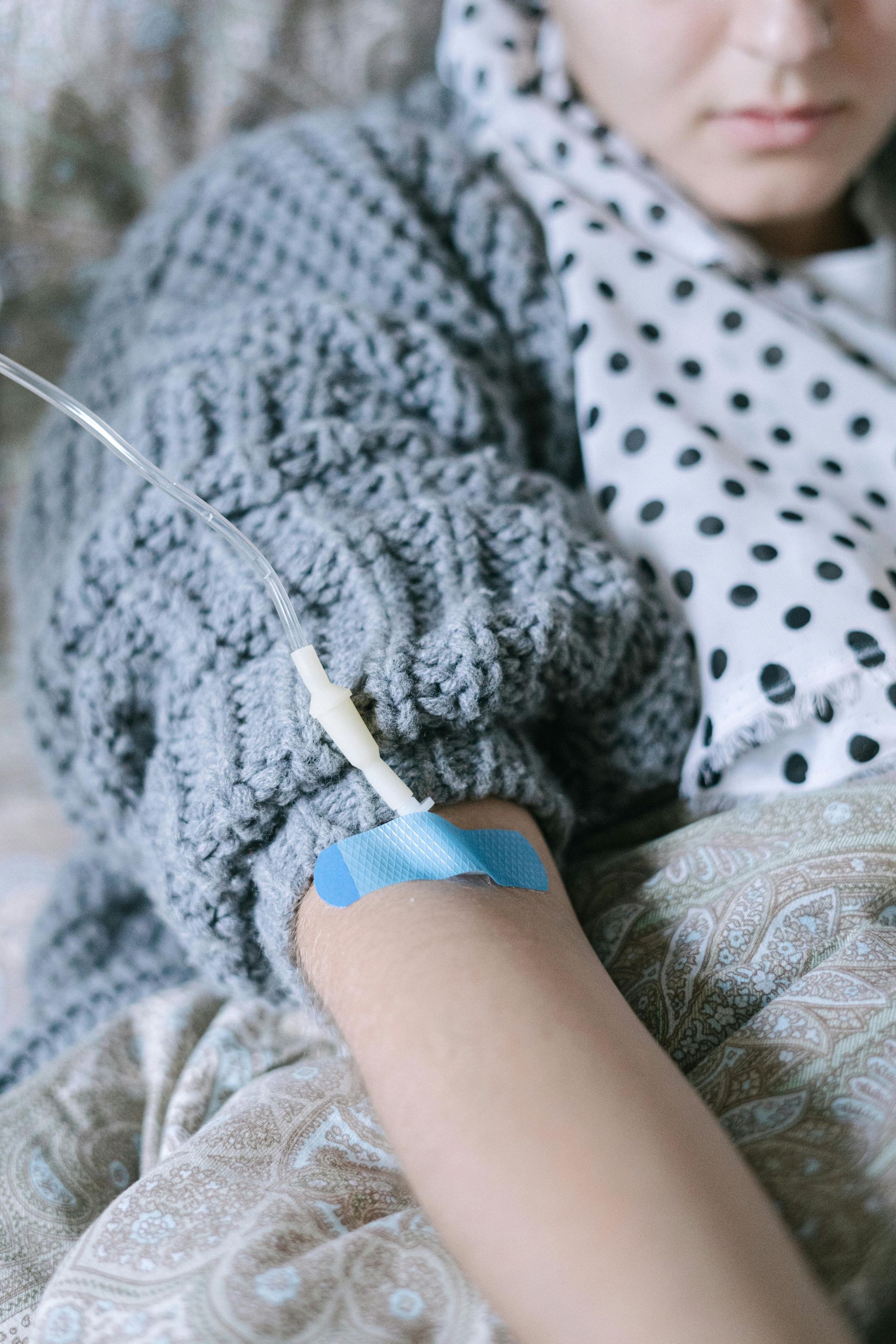 A woman is laying in a hospital bed with an iv in her hand.