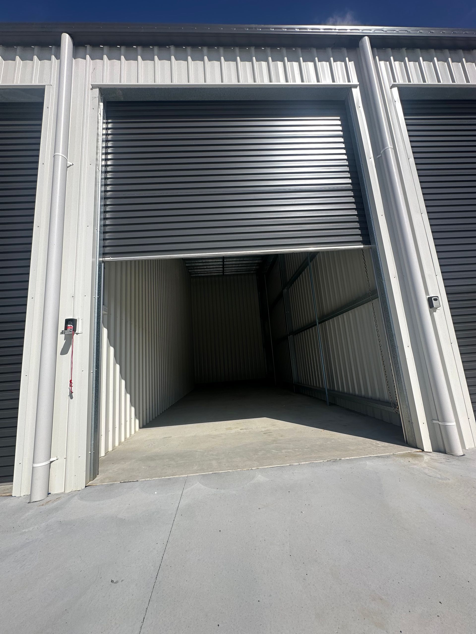 Partially Open Metal Roll-up Warehouse Door Revealing A Dim Storage Unit — Midcoast Premium Caravan Storage in Forster, NSW