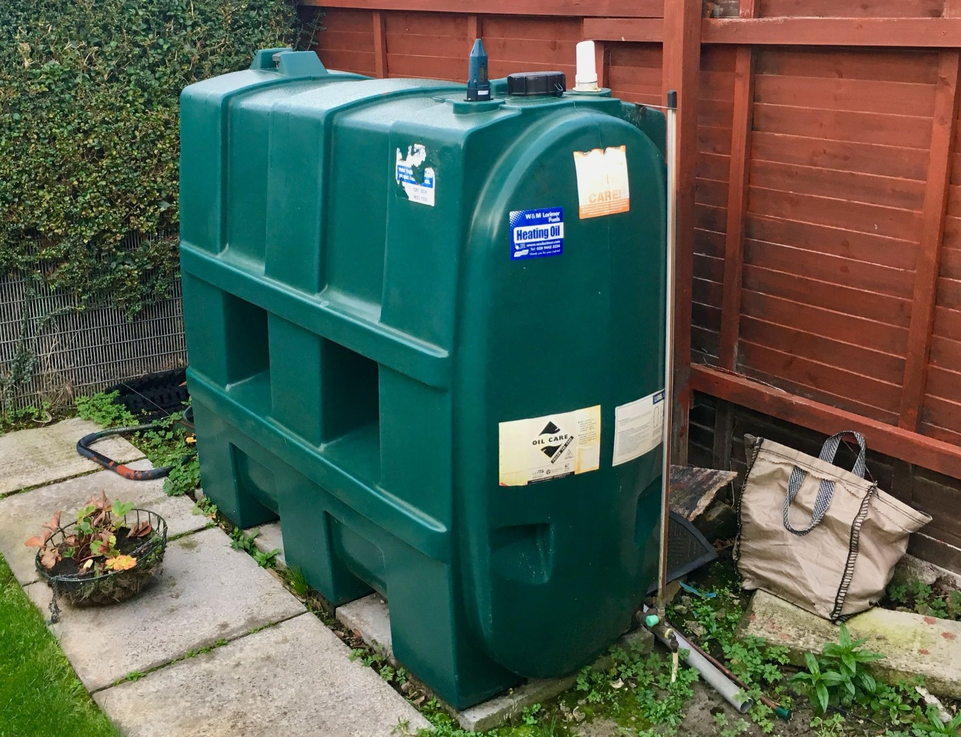 A photograph of a life-expired Harlequin 1100SL Single Skin Oil Tank, installed in a garden.