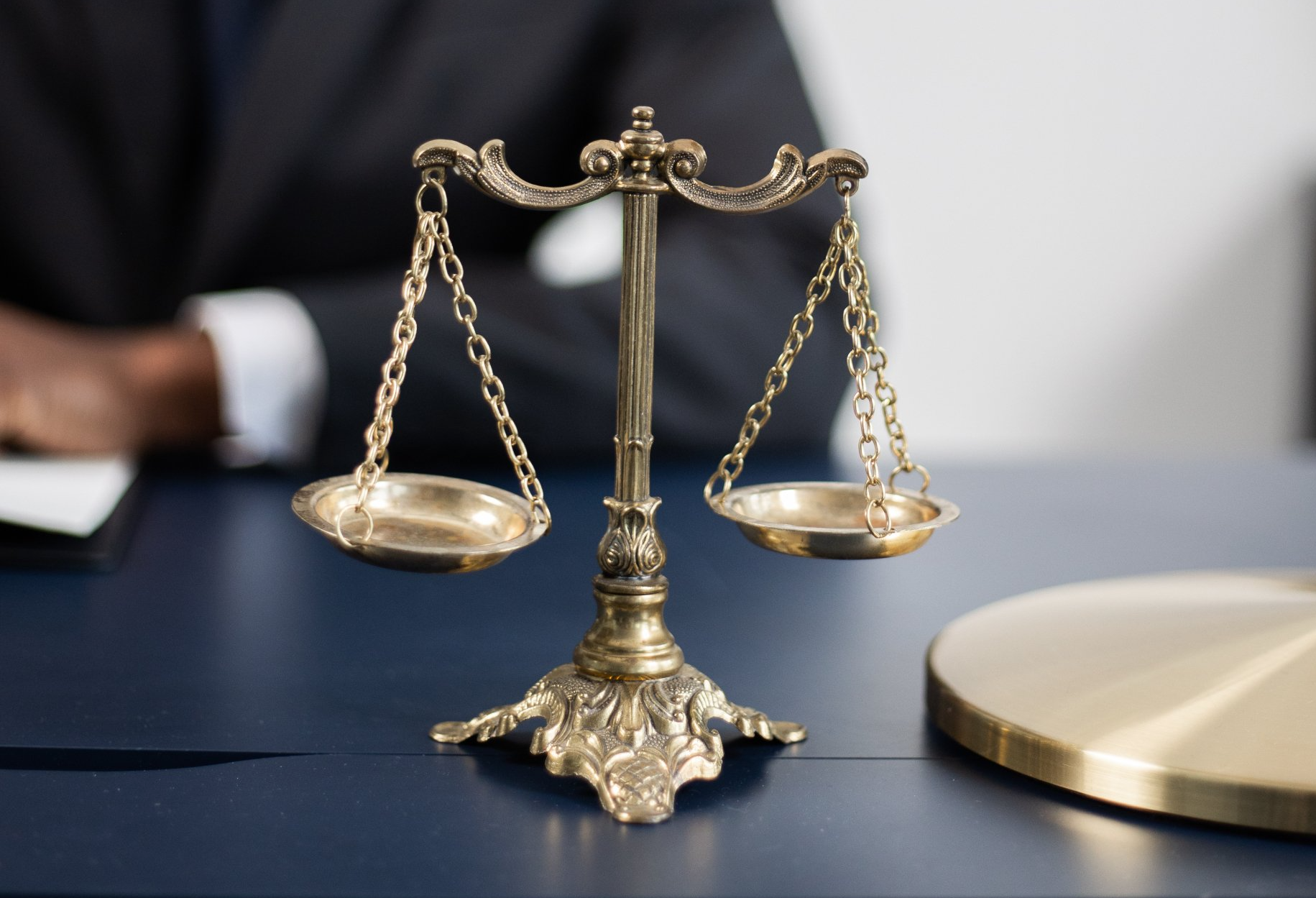 A scale of justice is sitting on a table in front of a man in a suit.