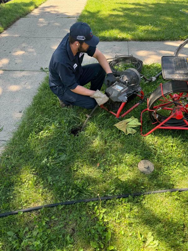 Plumber working on a sewer line in a yard, using equipment.