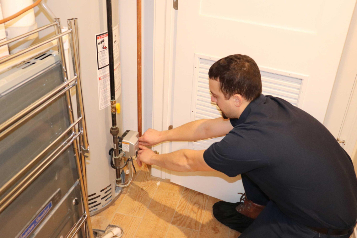 Plumber kneeling, working on a water heater near a white door, indoors.