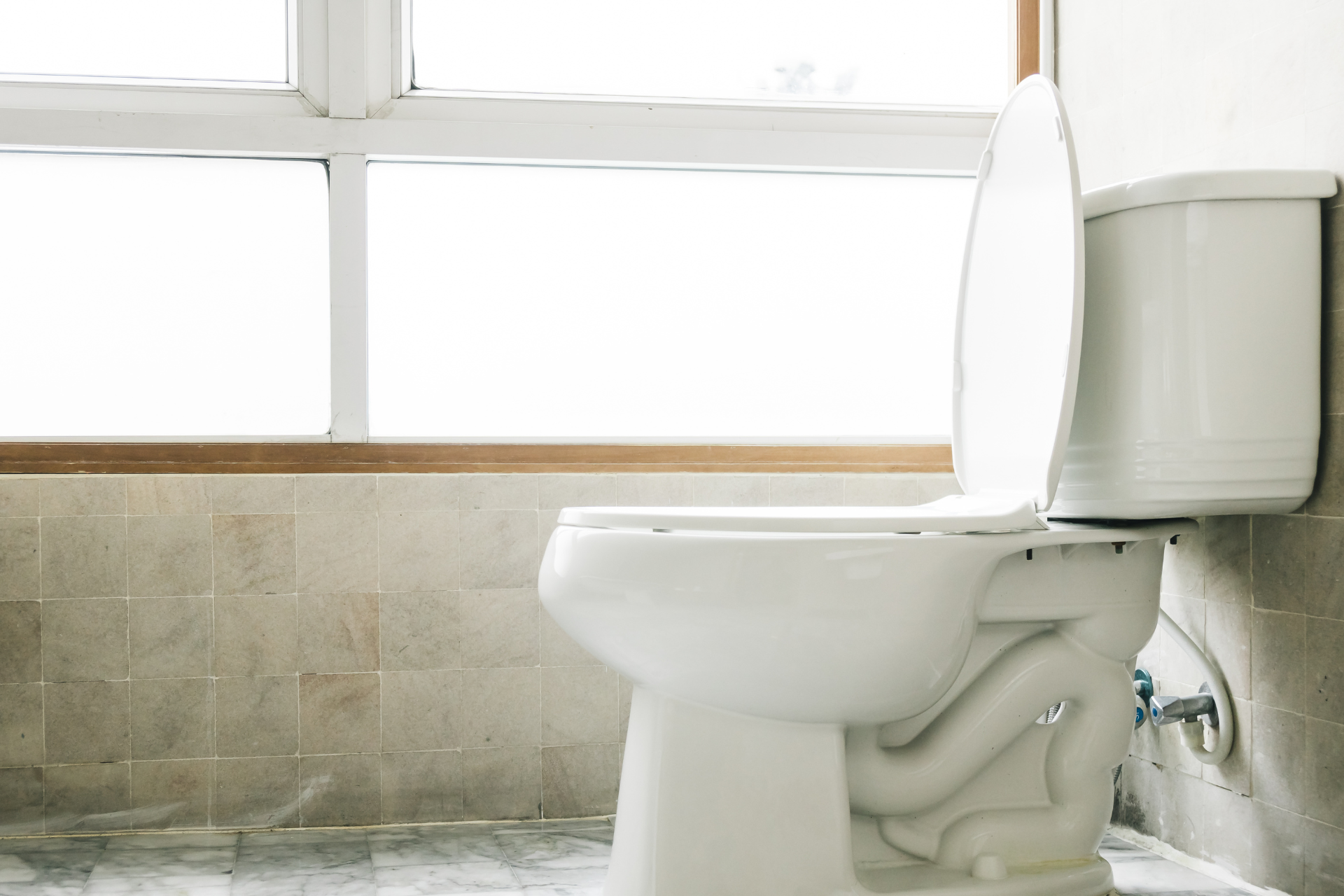 White toilet with open lid in a bathroom. Window and tiled wall are in the background.