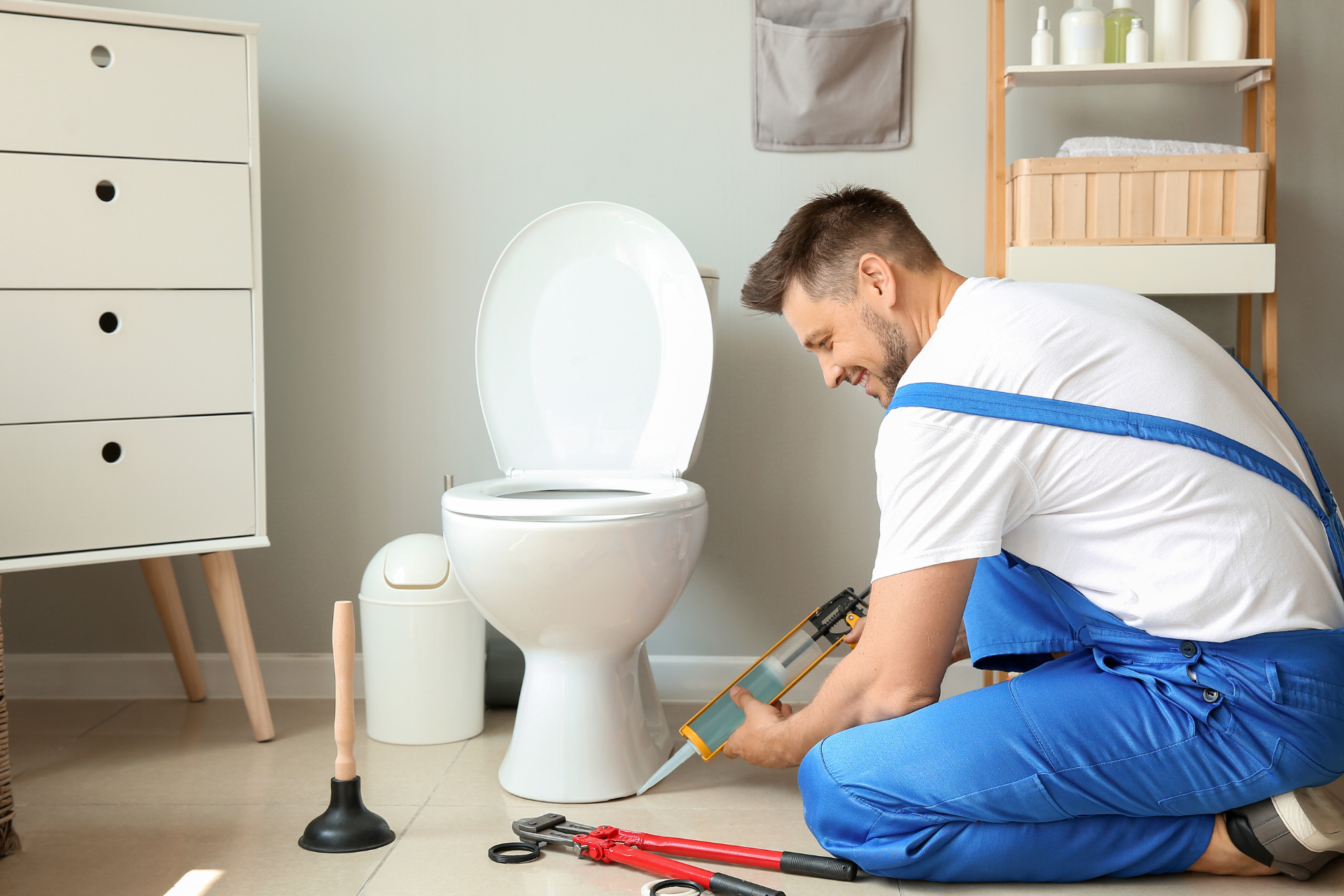 Plumber caulking around a toilet in a bathroom, smiling.