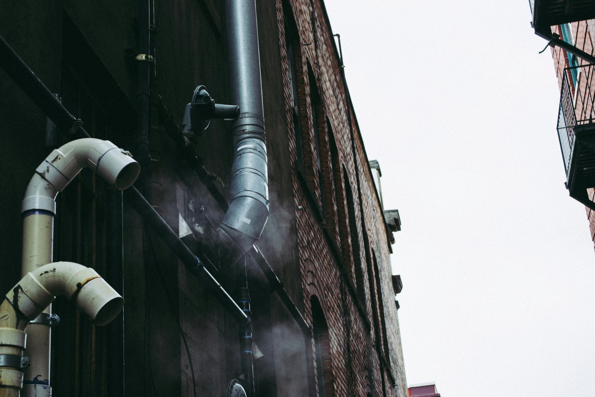 Brick building exterior with pipes and a cloudy sky.