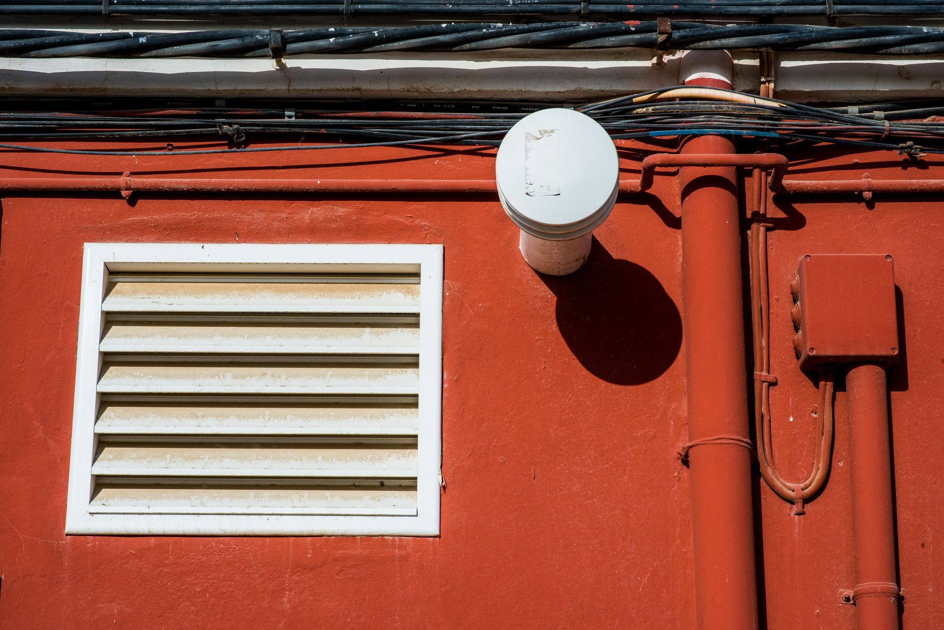 Red wall with white-framed vent, round vent and pipes, electrical box.