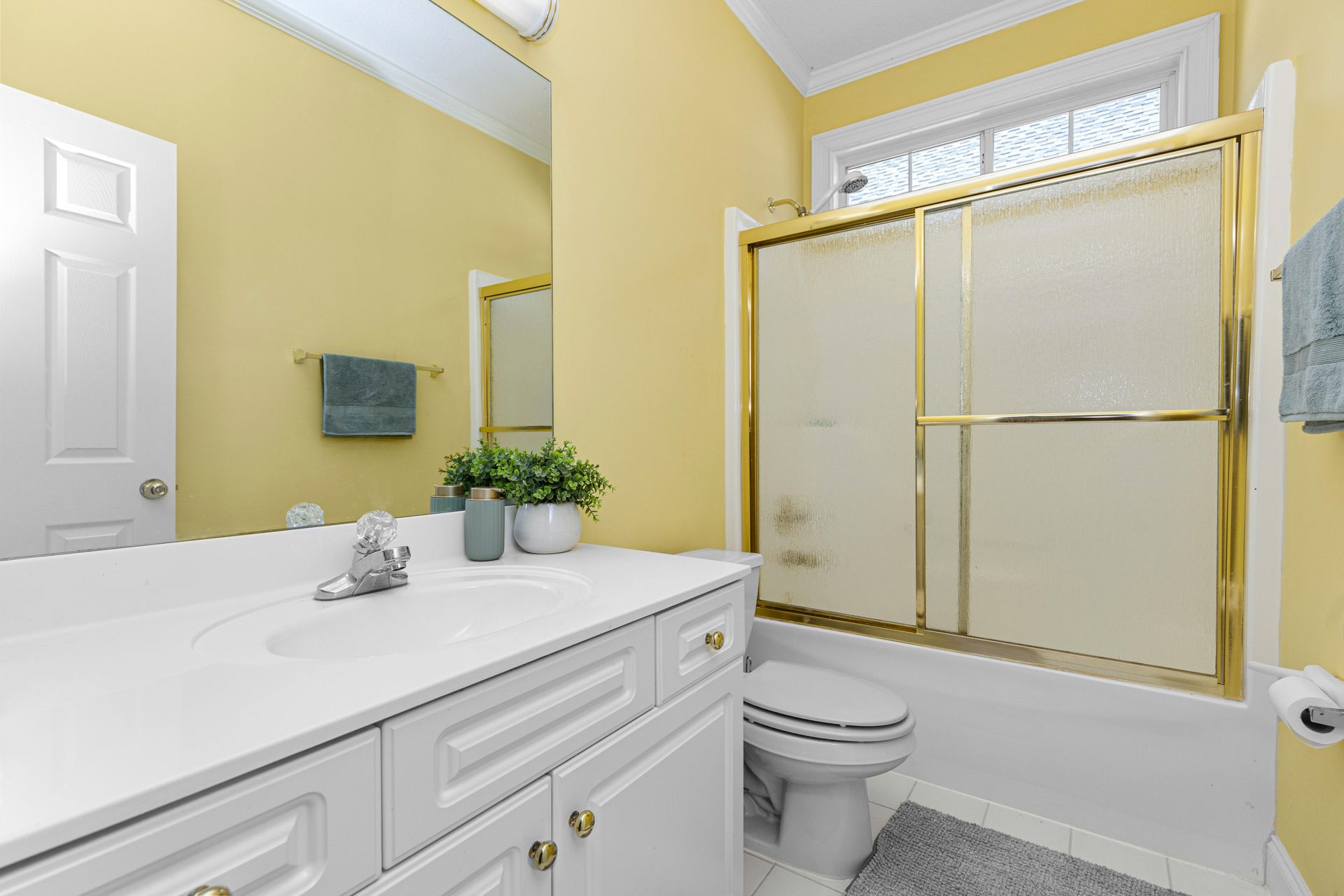 Bathroom with white vanity, yellow walls, gold shower door, and toilet.