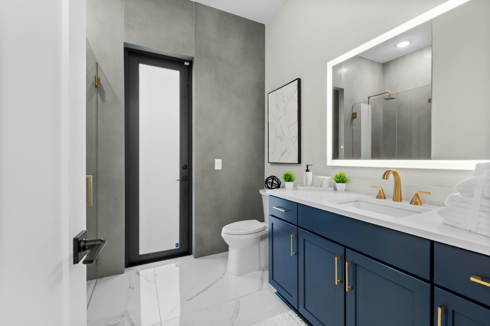 Modern bathroom with blue vanity, gold fixtures, and a large mirror.