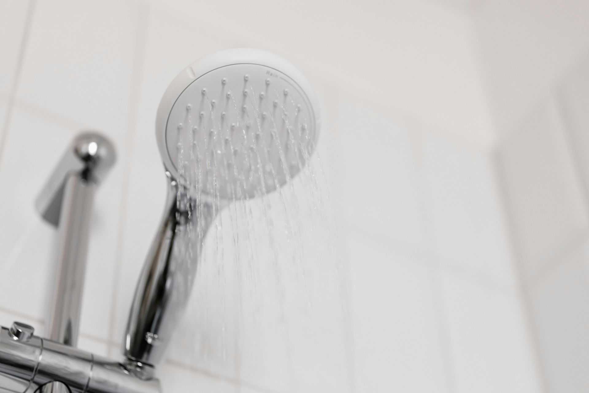 Showerhead spraying water; white tile background.