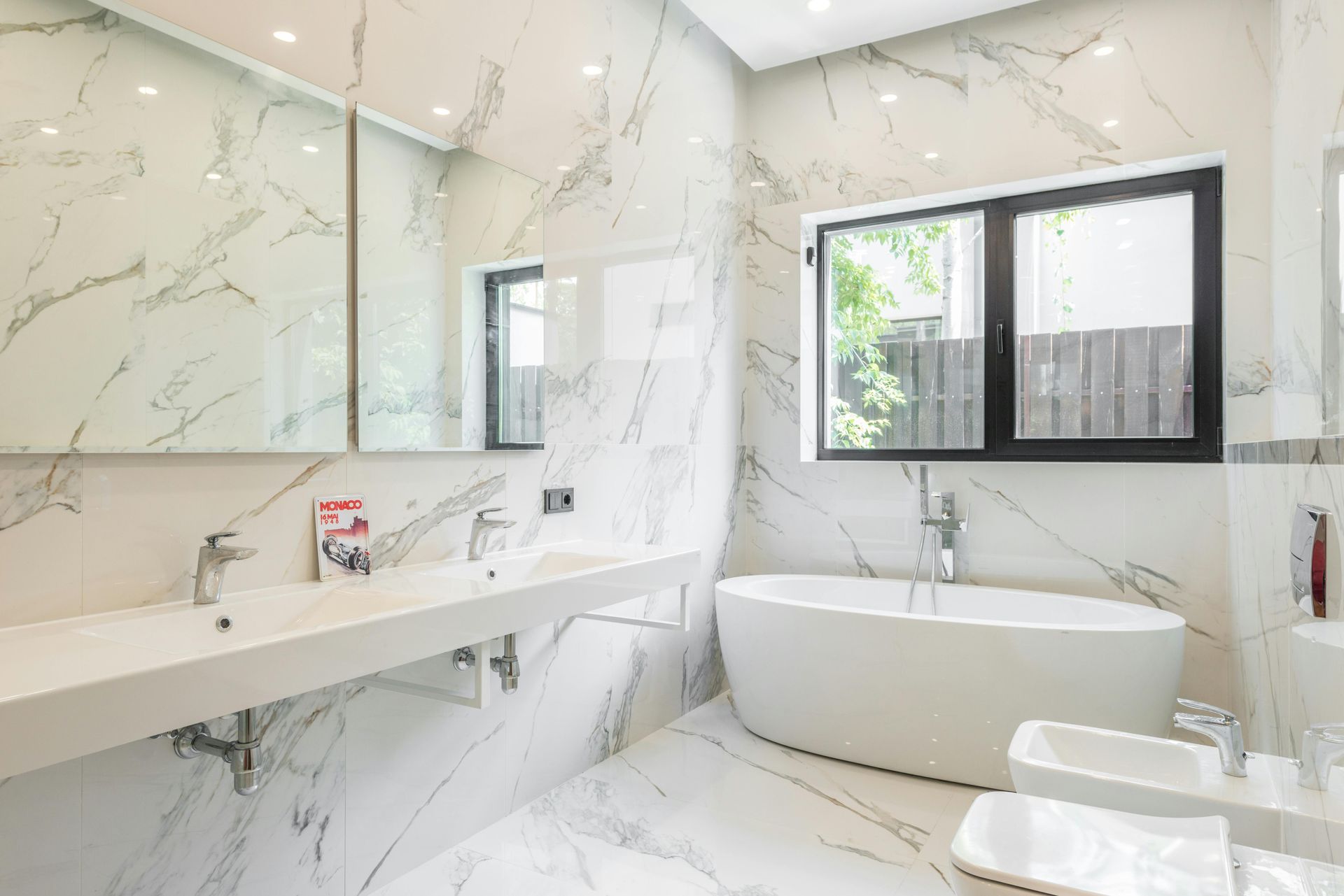 Modern bathroom with marble-look tile, a white tub, double sinks, and a window with a view.