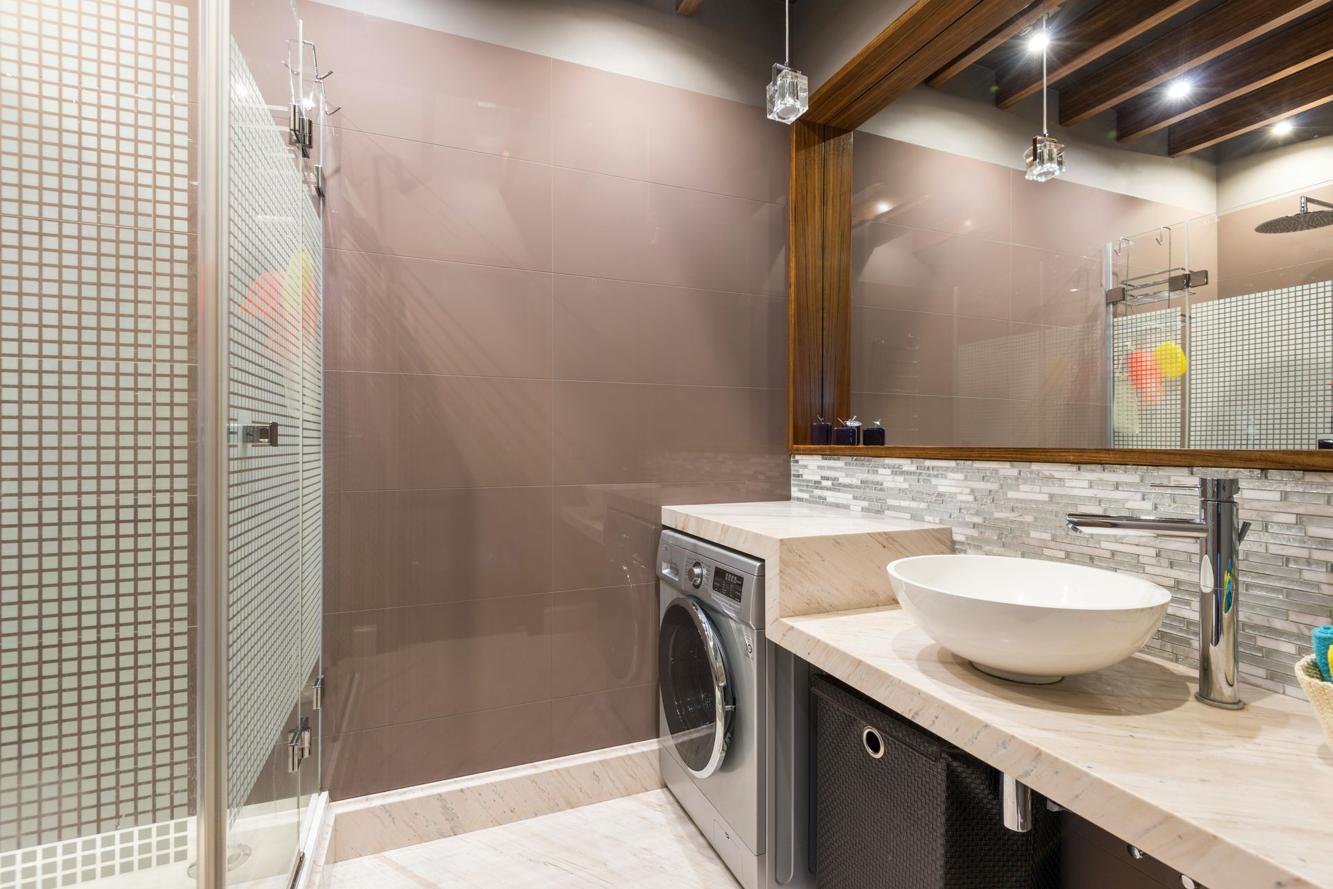 Bathroom with a shower, washing machine, sink, and mirror. Brown, beige, and gray tones.