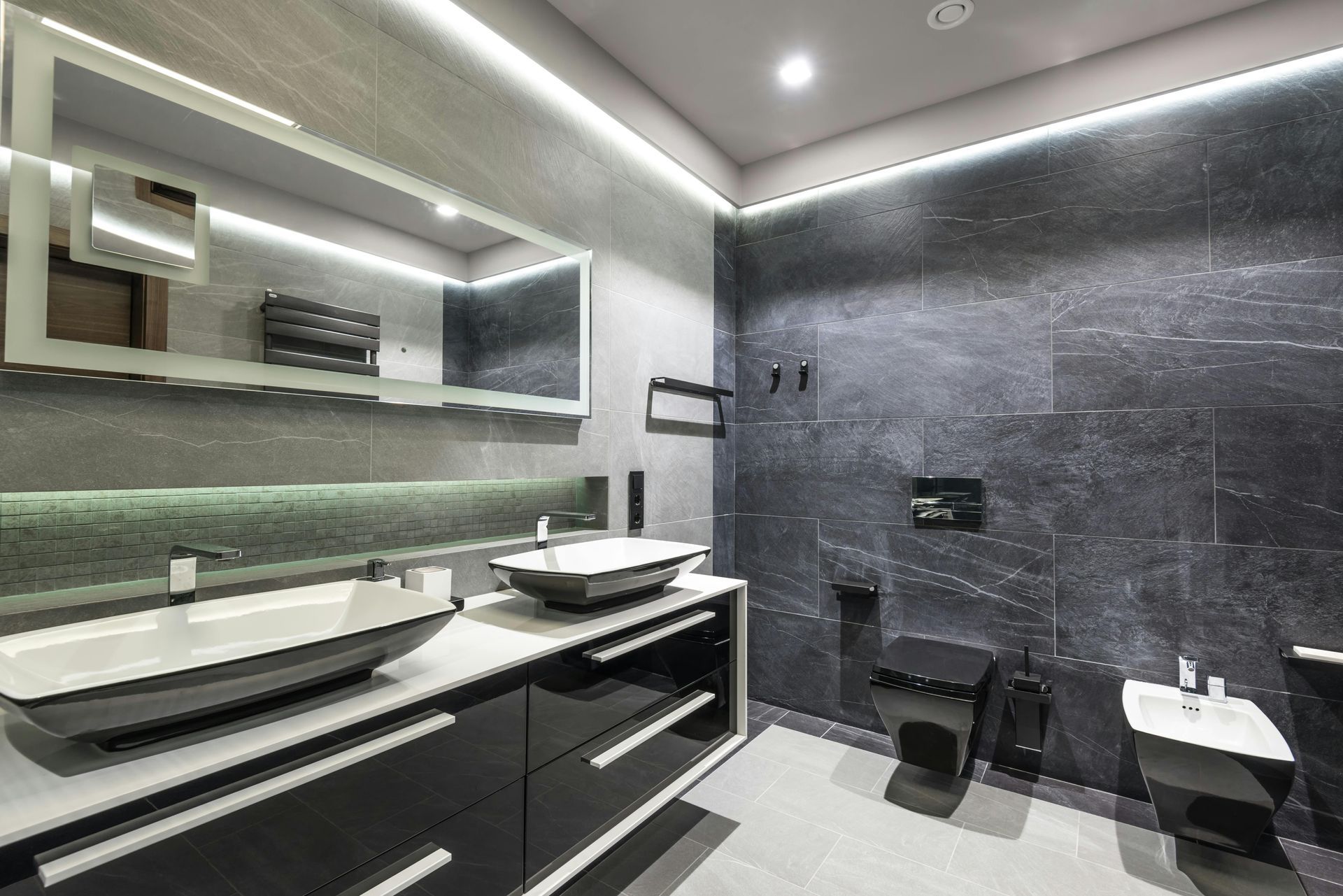 Modern bathroom with dark gray tile walls, black vanity, and white sinks.