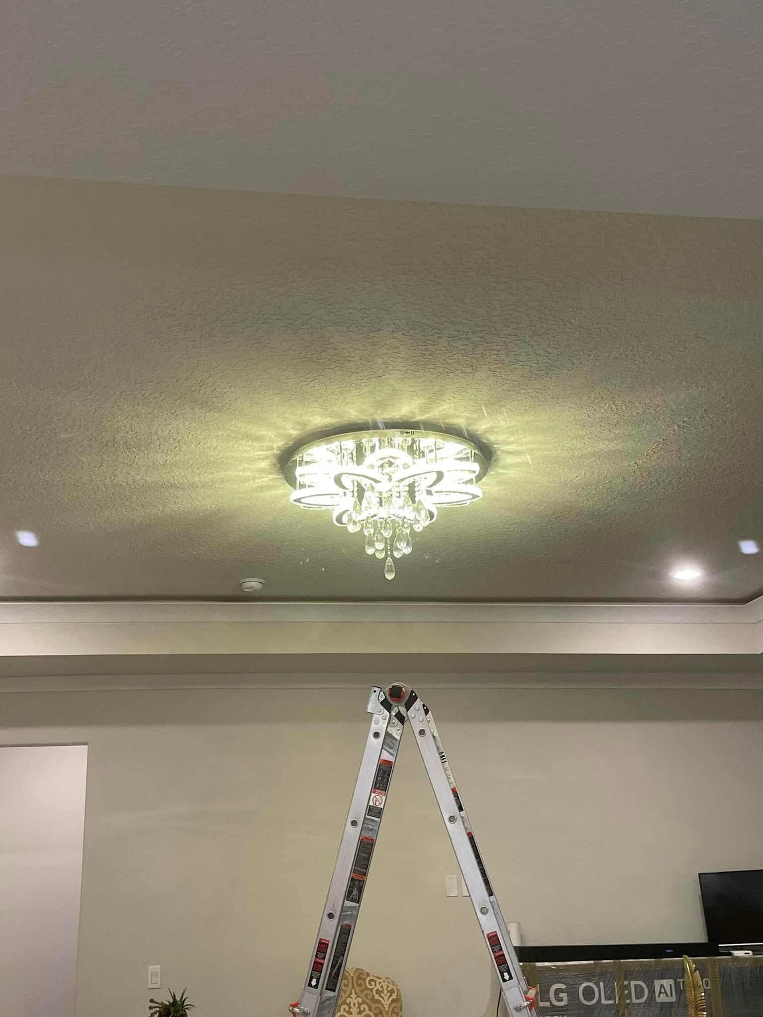 Ceiling chandelier above a ladder in a room with recessed lights and a textured ceiling.