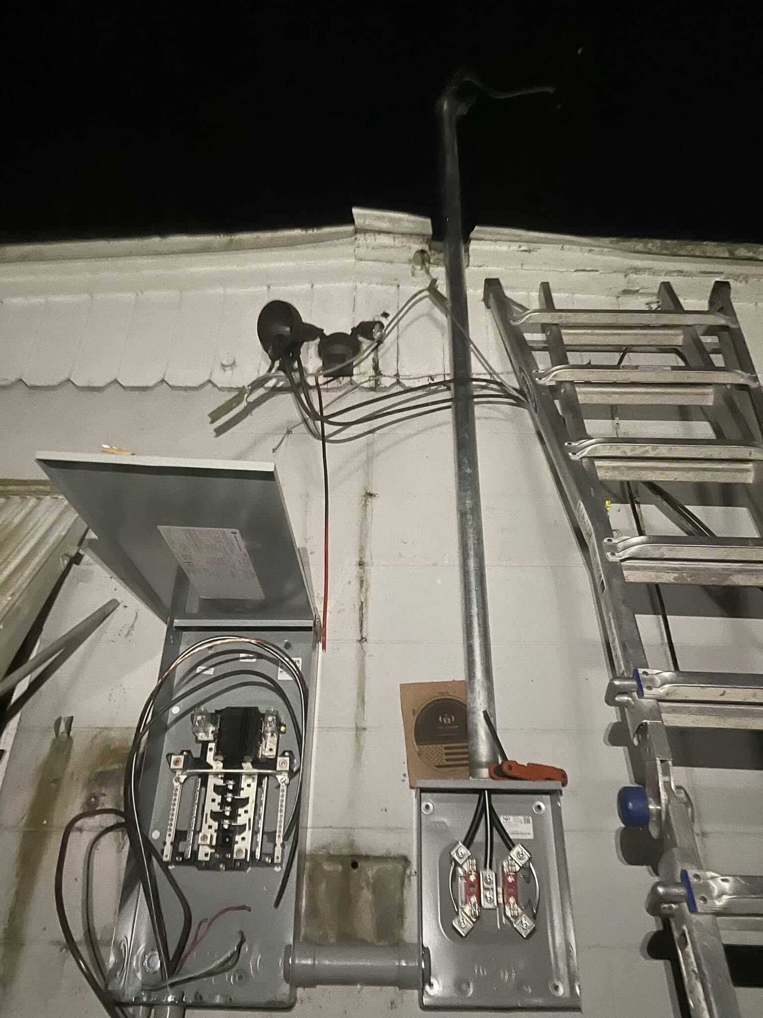 Nighttime view of a building wall with cables, a ladder, and an electrical box under harsh light