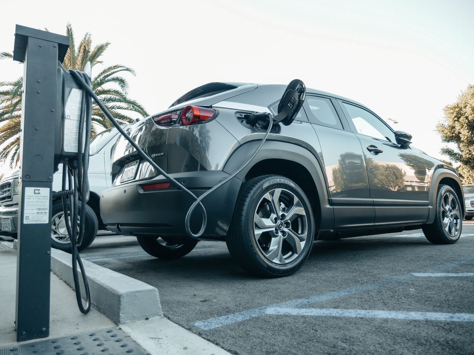 Gray electric SUV charging at a station in a parking lot, with cable connected to the rear