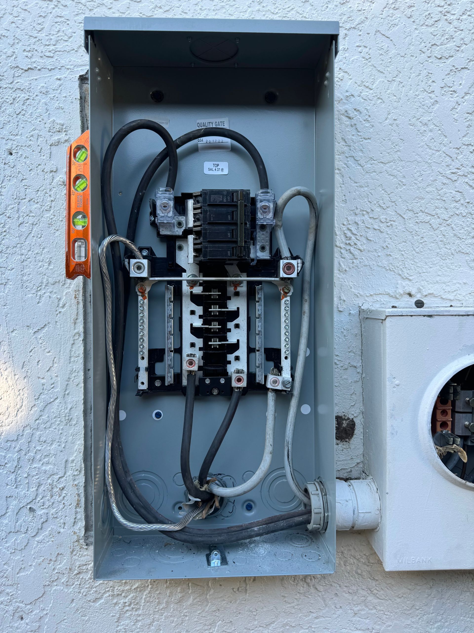 Open electrical breaker panel in a gray metal box mounted on a stucco wall.