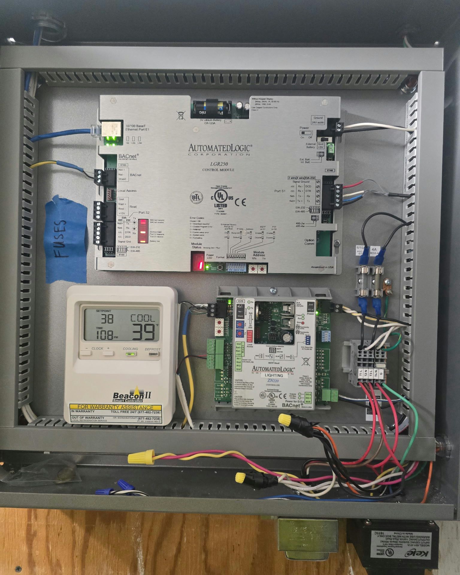 Open electrical control panel with meters, wiring, and circuit boards mounted inside a metal cabinet.