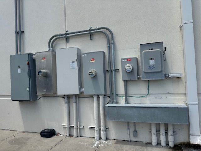 Gray electrical utility boxes and conduits mounted on an exterior building wall.