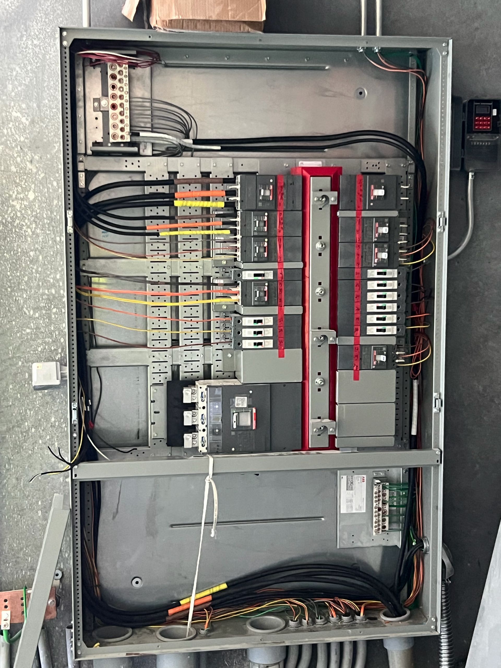 Open electrical control panel with wiring, breakers, and red circuit modules inside a metal cabinet