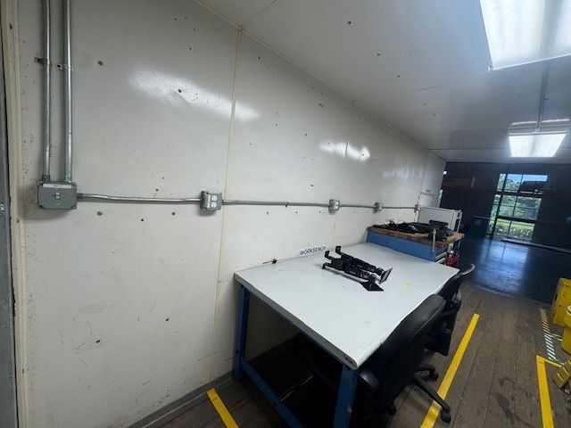Industrial hallway with a tilted white workbench, wall conduit, and yellow floor markings