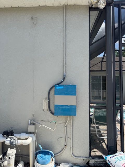 Blue utility box mounted on a gray exterior wall with pipes and cables attached