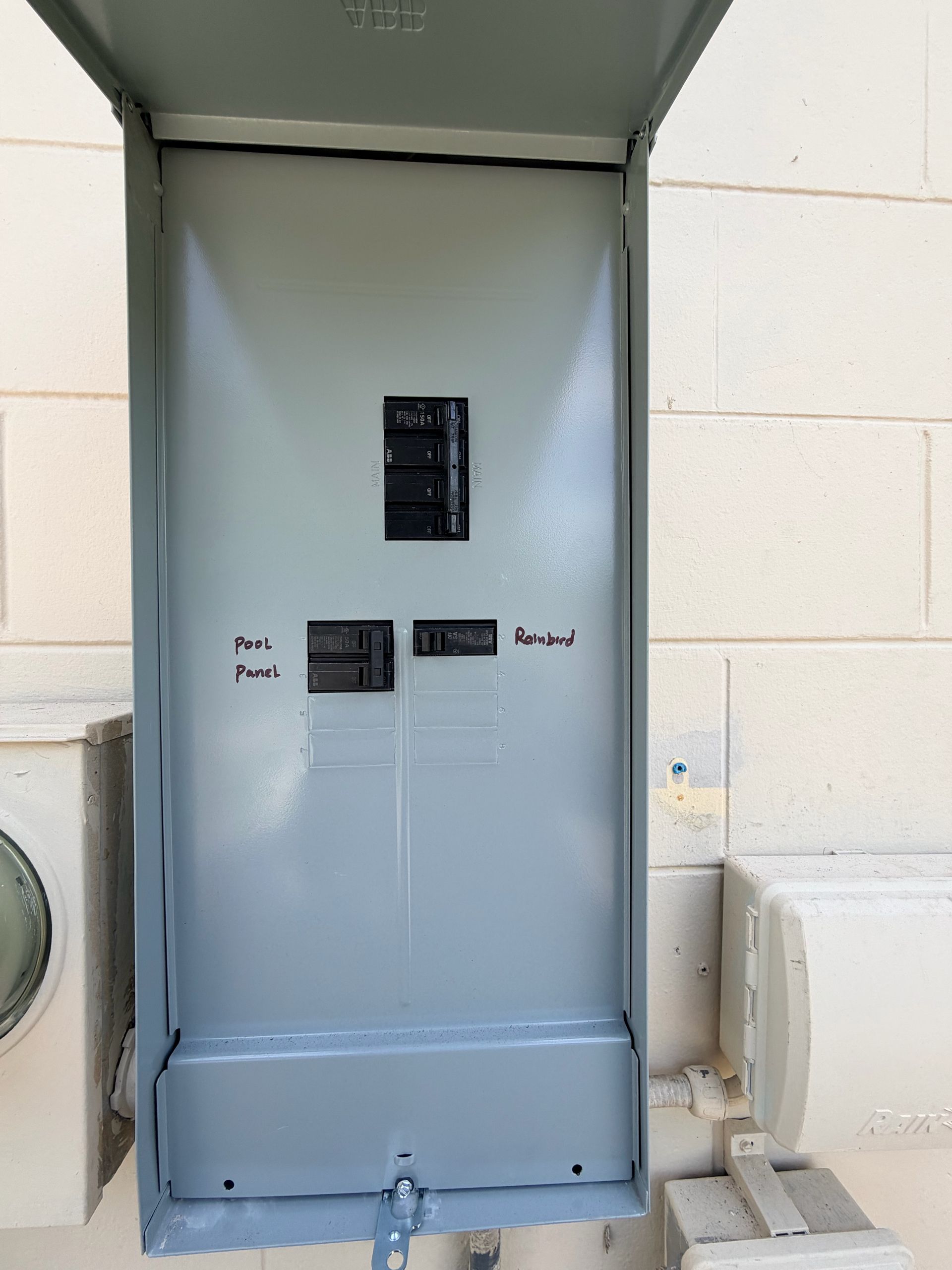 Open electrical panel on a wall with circuit breakers and a gray cover door