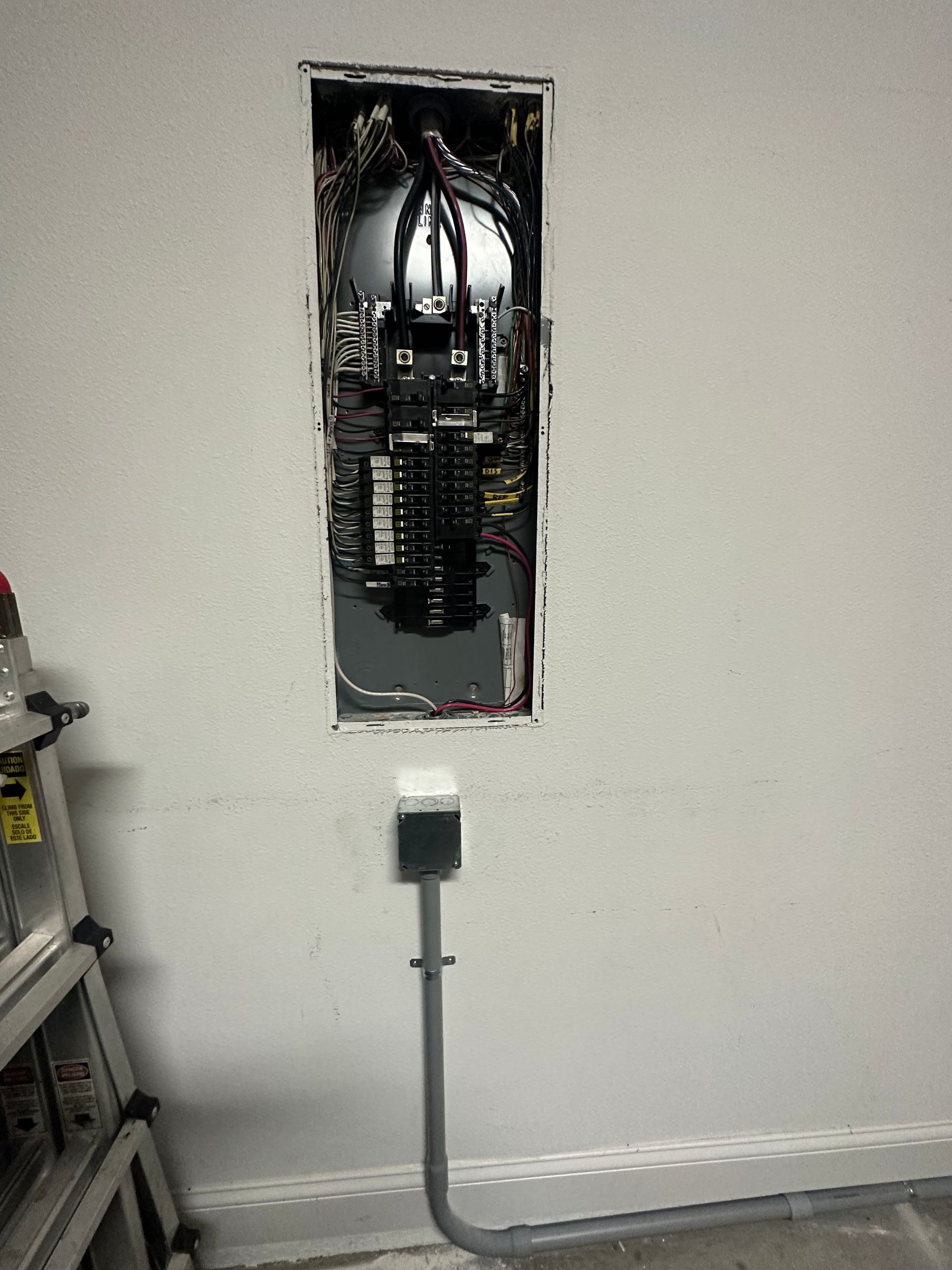 Open electrical breaker panel with exposed wiring and cover removed on a wall.