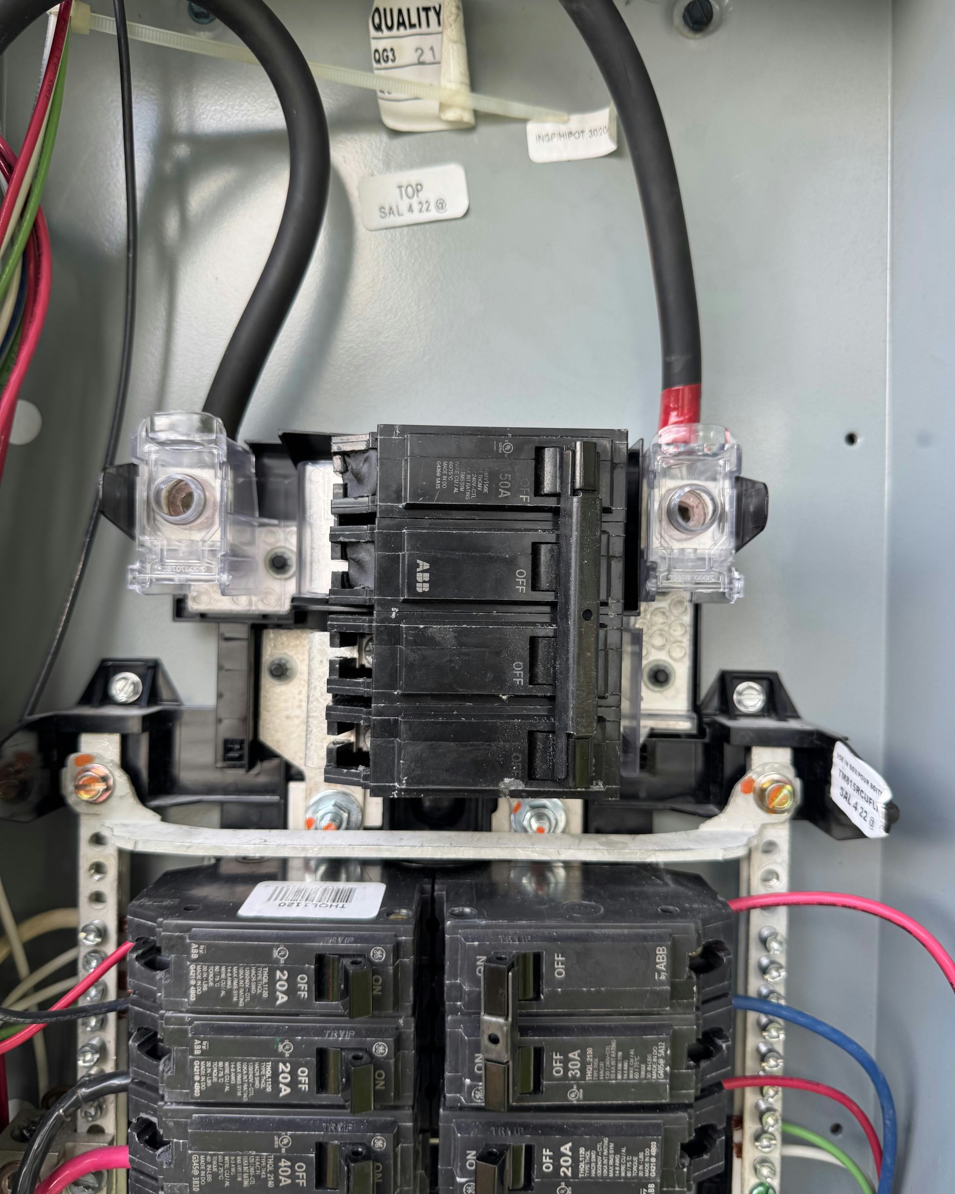 Electrical breaker panel with black circuit breakers and thick red and black wires.