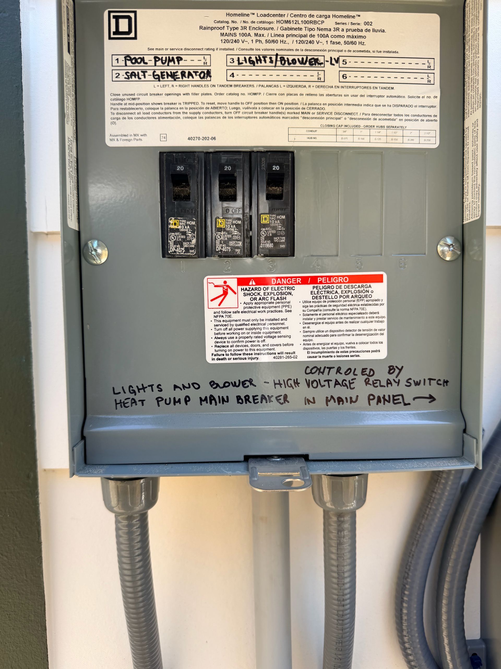 Electrical breaker panel with warning labels and conduit pipes entering the bottom.