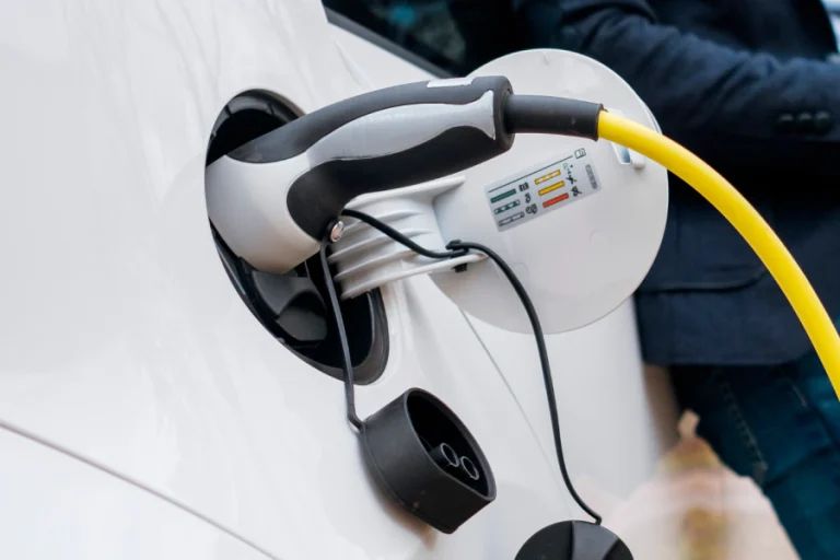 White electric vehicle charging plug inserted into a car’s charging port, with a yellow cable attached