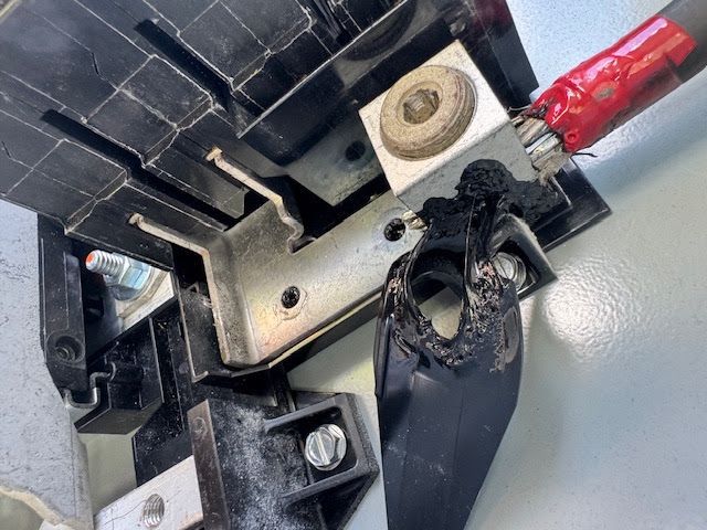 Close-up of a damaged black plastic part and metal hardware with a red wire attached.