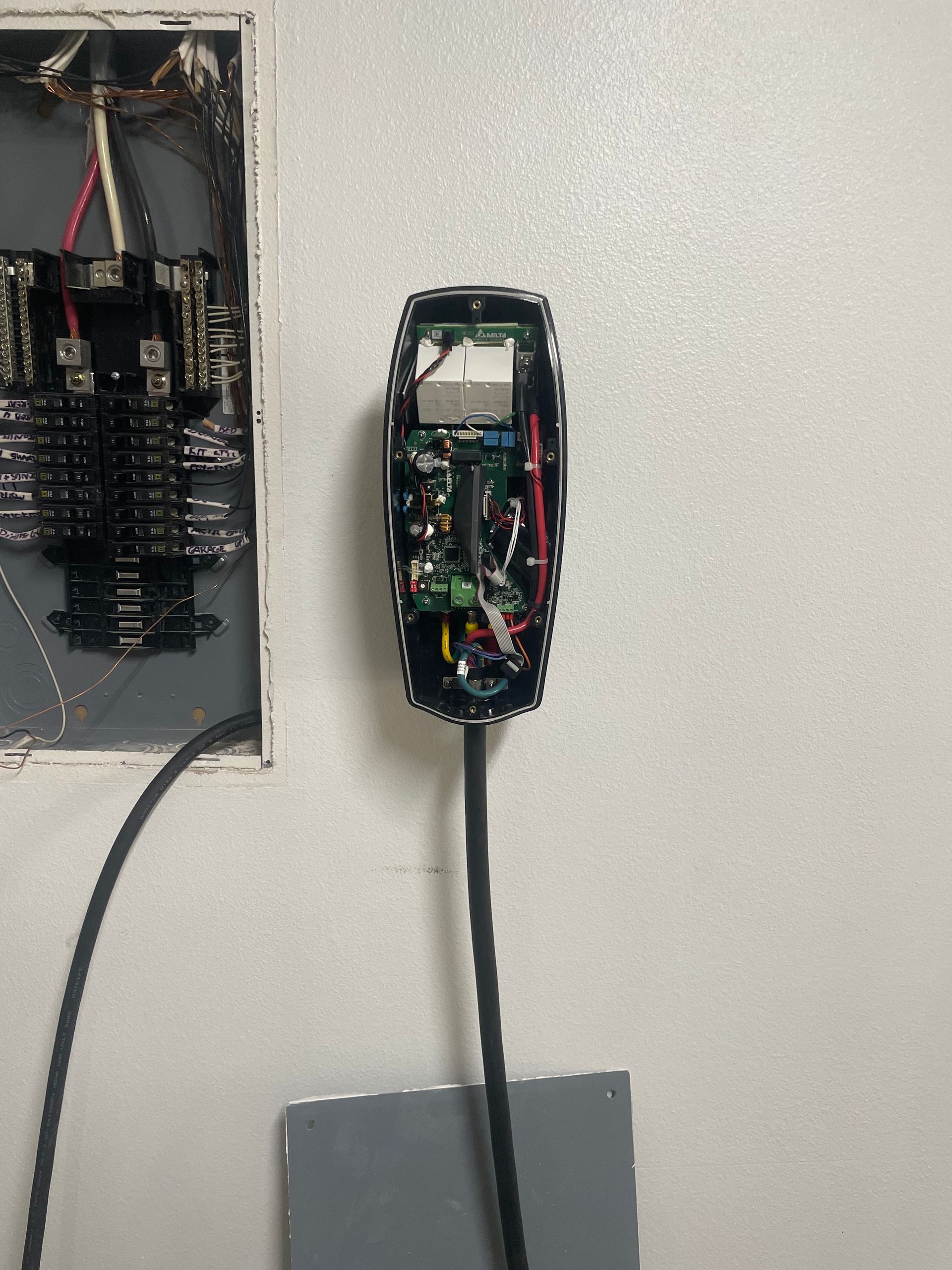 Open electrical boxes with exposed wiring on a light wall, one above a gray floor cabinet.