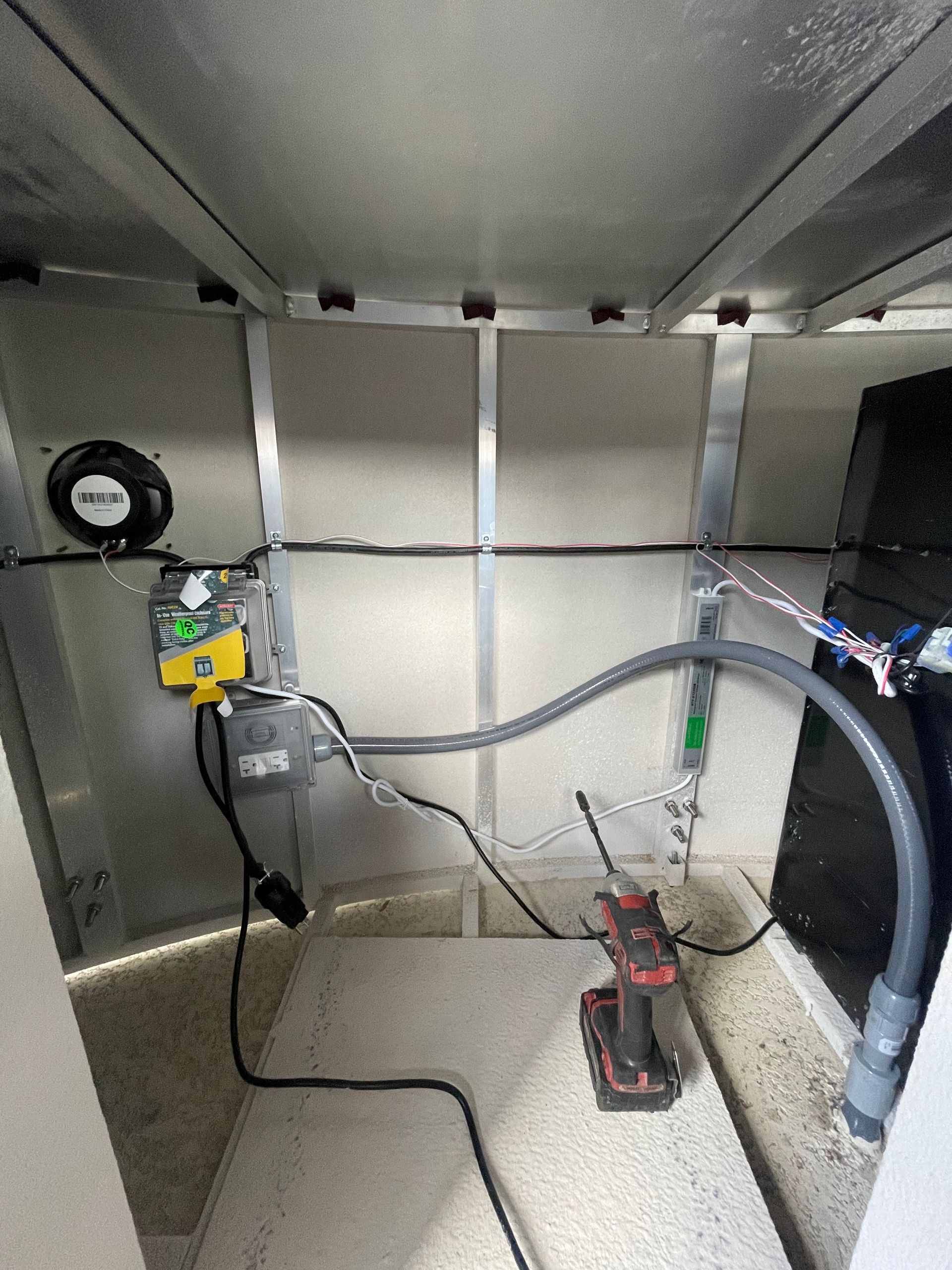 Inside a metal electrical cabinet with wiring, gauges, and a red clamp meter on the floor