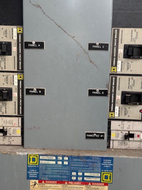 Electrical breaker panel with labeled switches and a large gray center cover.