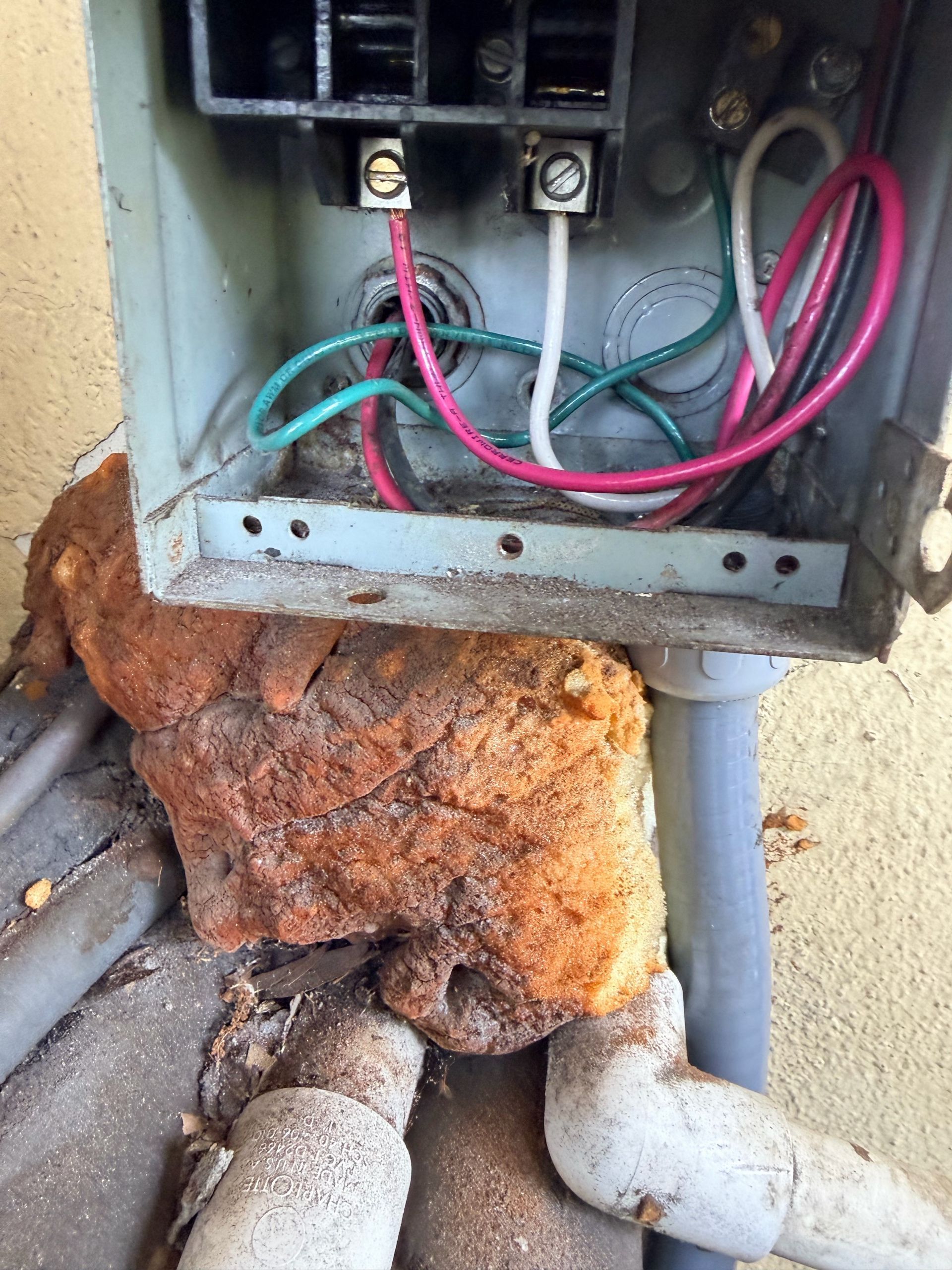 Damaged electrical box with exposed wires and heavy rust corrosion near pipes.