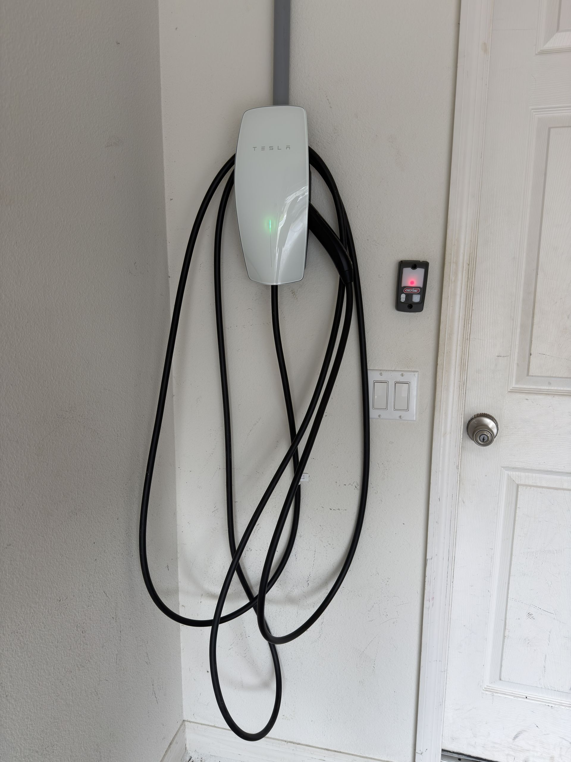 Wall-mounted EV charger with coiled black cable beside a door in a hallway