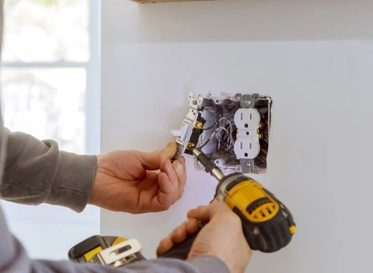 Hands wiring an electrical outlet box with a drill in a wall.