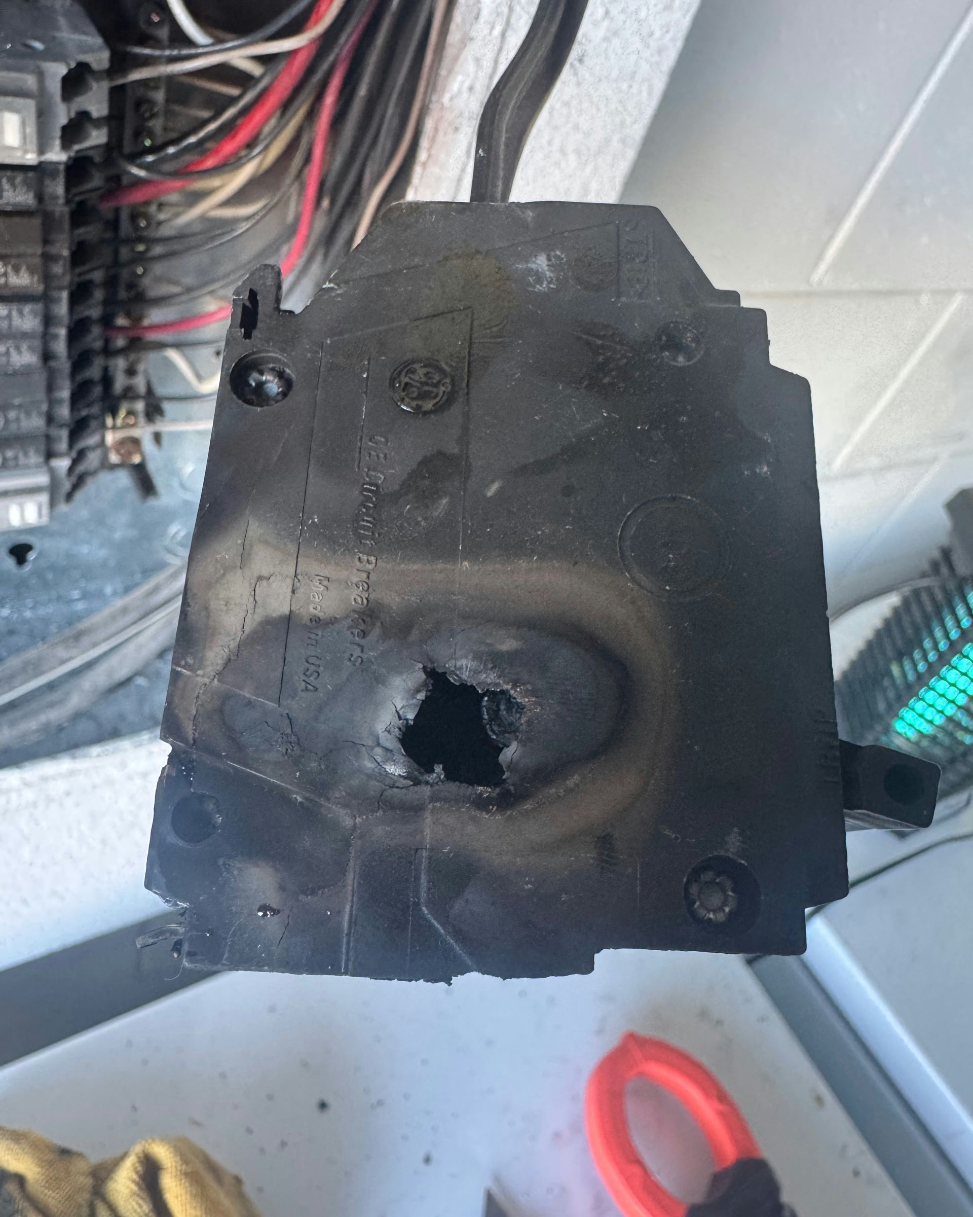 Black plastic electrical box with a burnt hole, mounted among wires inside a panel.