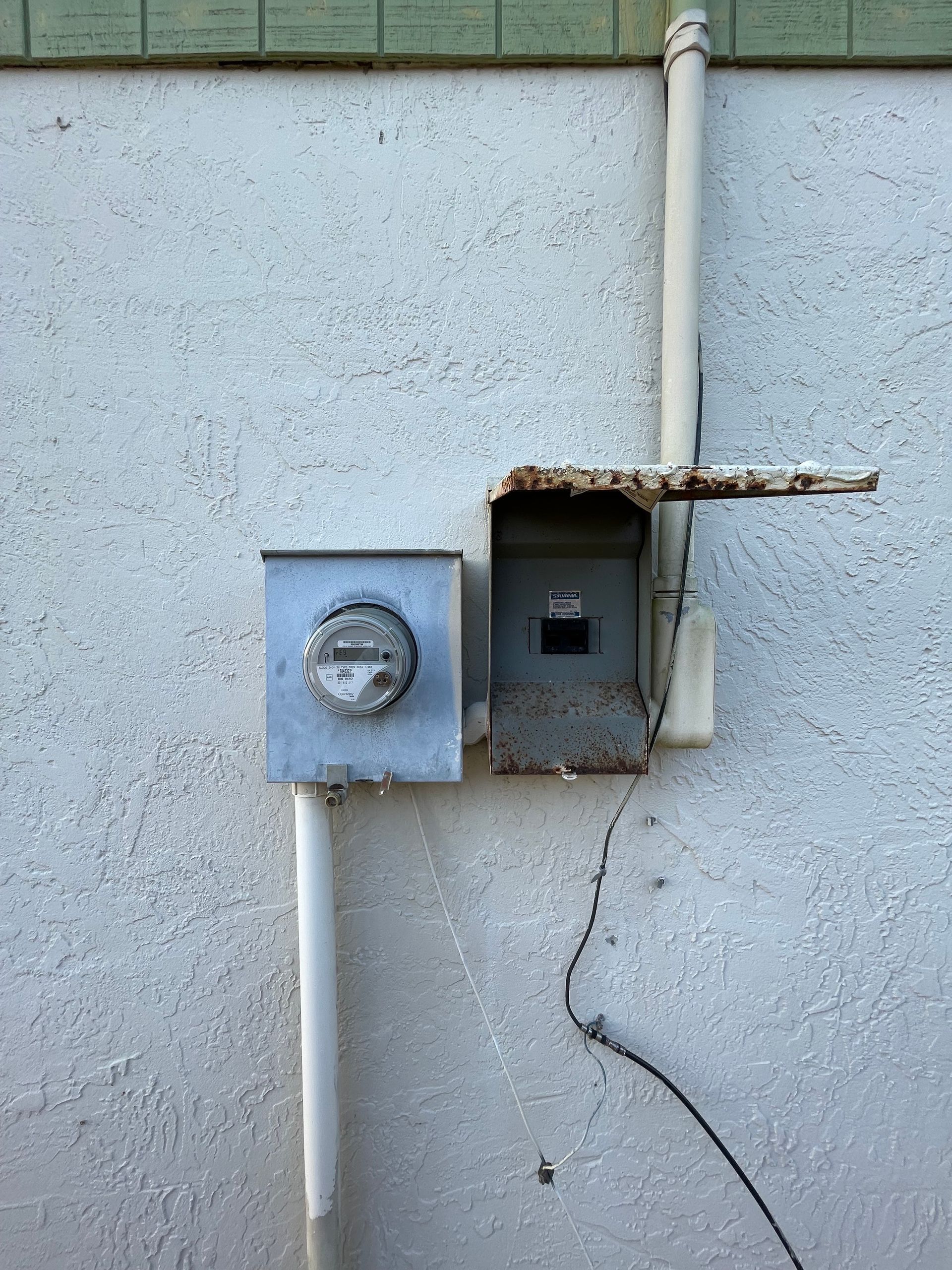 Two electrical meters on a stucco wall, with one cover open and a cracked section below