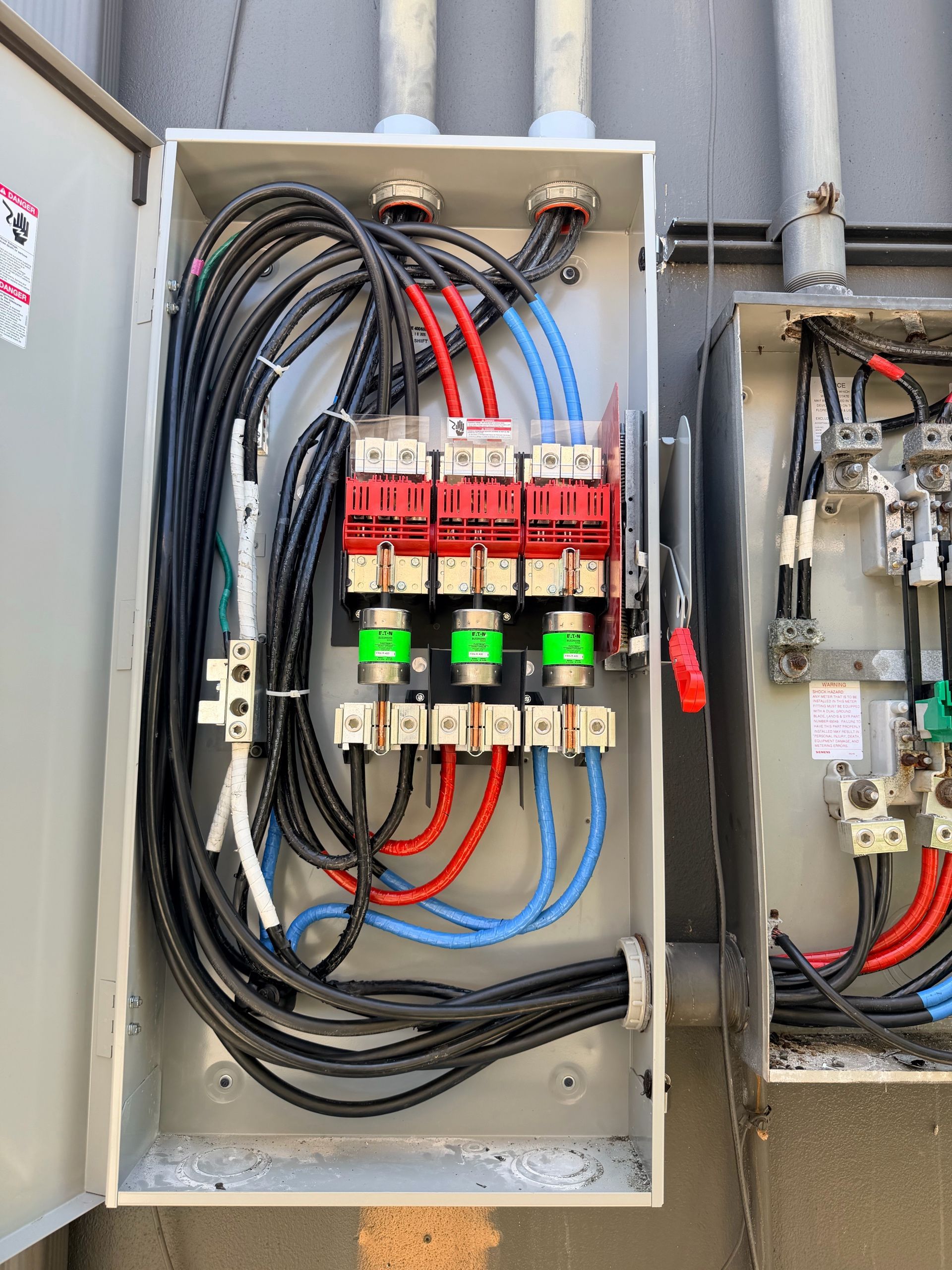 Electrical control panel with neatly wired red, blue, and black cables and circuit breakers in a metal enclosure